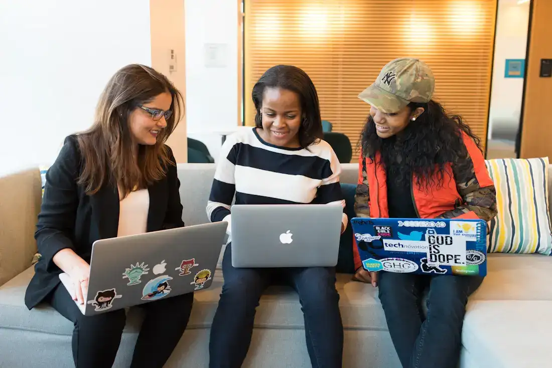 Three women working on laptops together on a sofa
