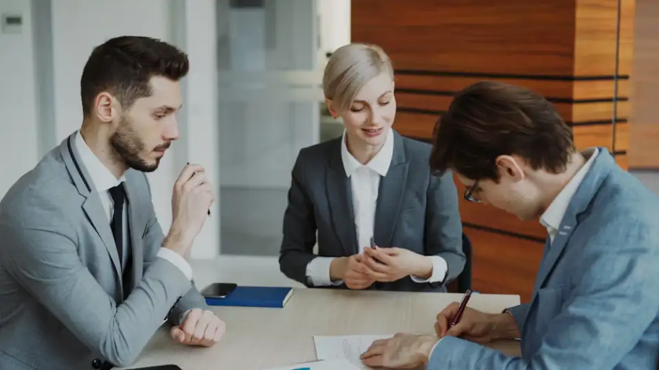 Three professionals in a meeting, one taking notes